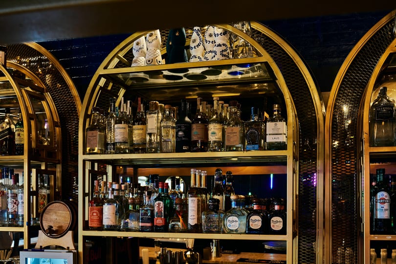 Well-stocked bar shelves with various tequila bottles and decorative ceramic pieces under warm lighting.