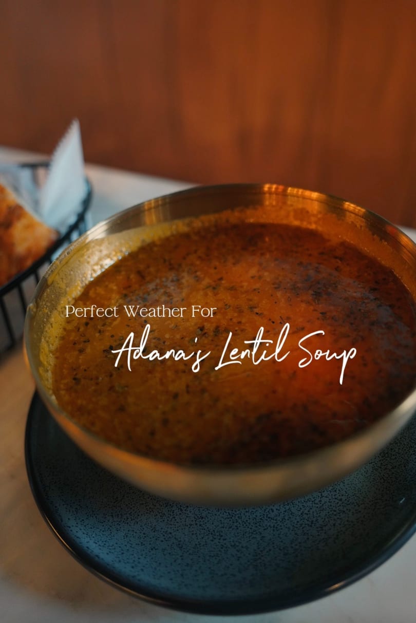 A golden bowl of Adana's lentil soup, garnished with herbs, on a speckled blue plate.